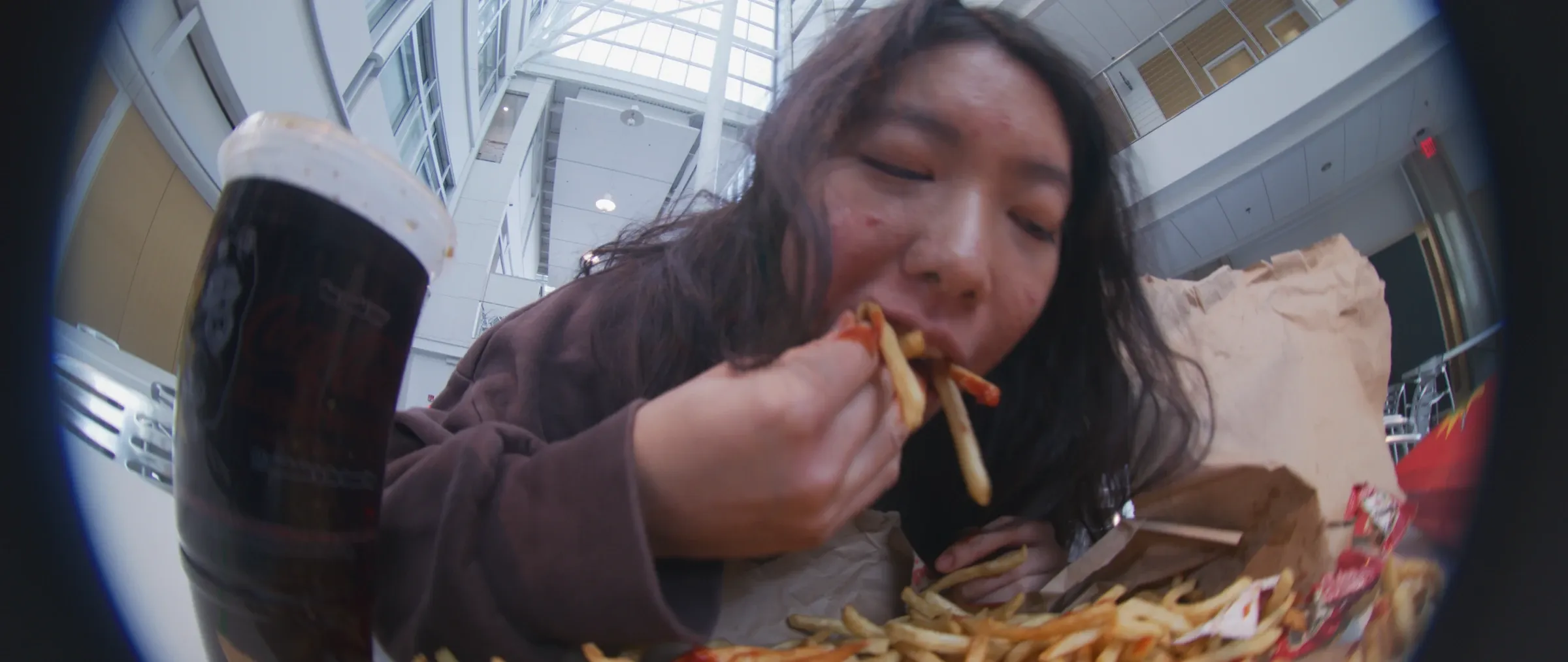 A woman eats fries in a bright atrium.