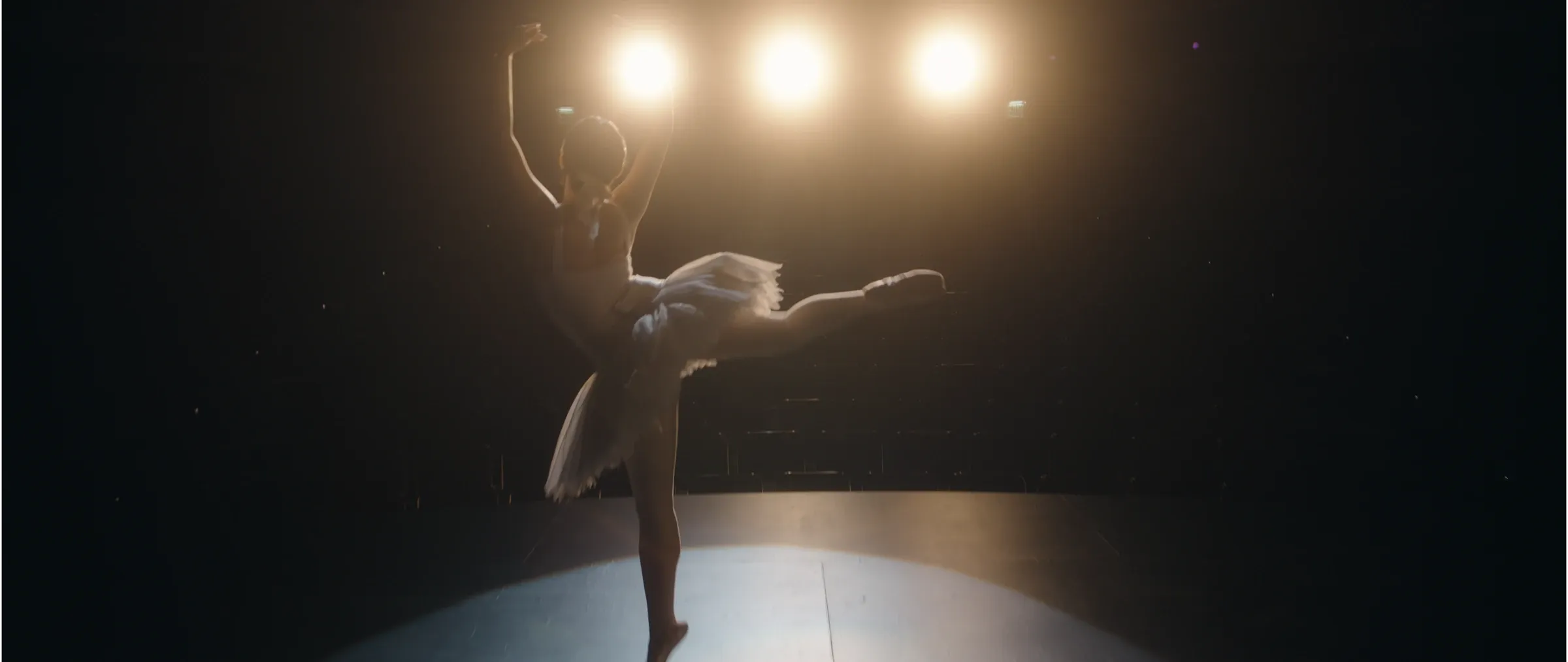 A ballerina performs beneath three stage lights.