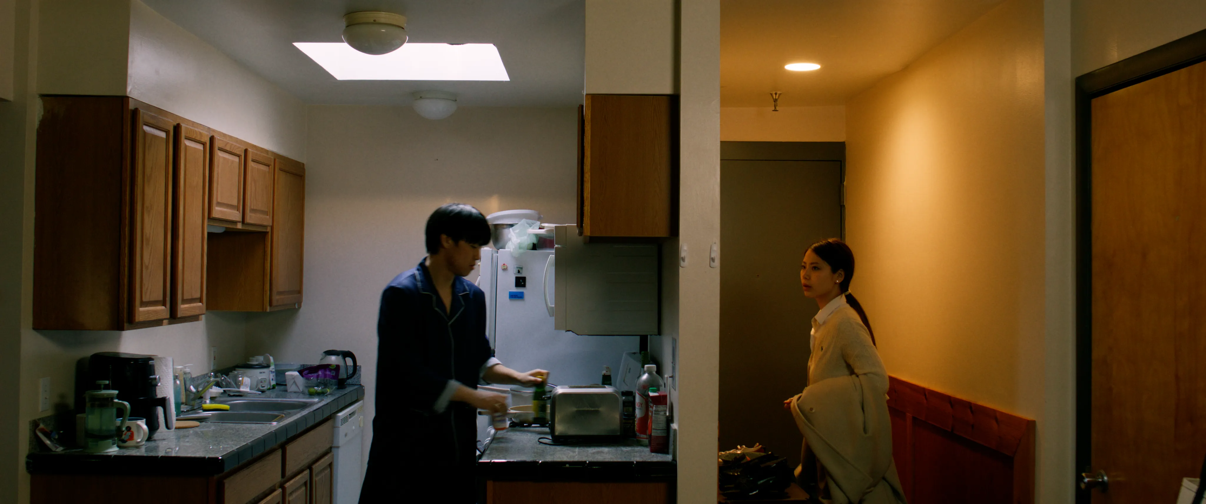 Two people in a kitchen and adjoining hallway.